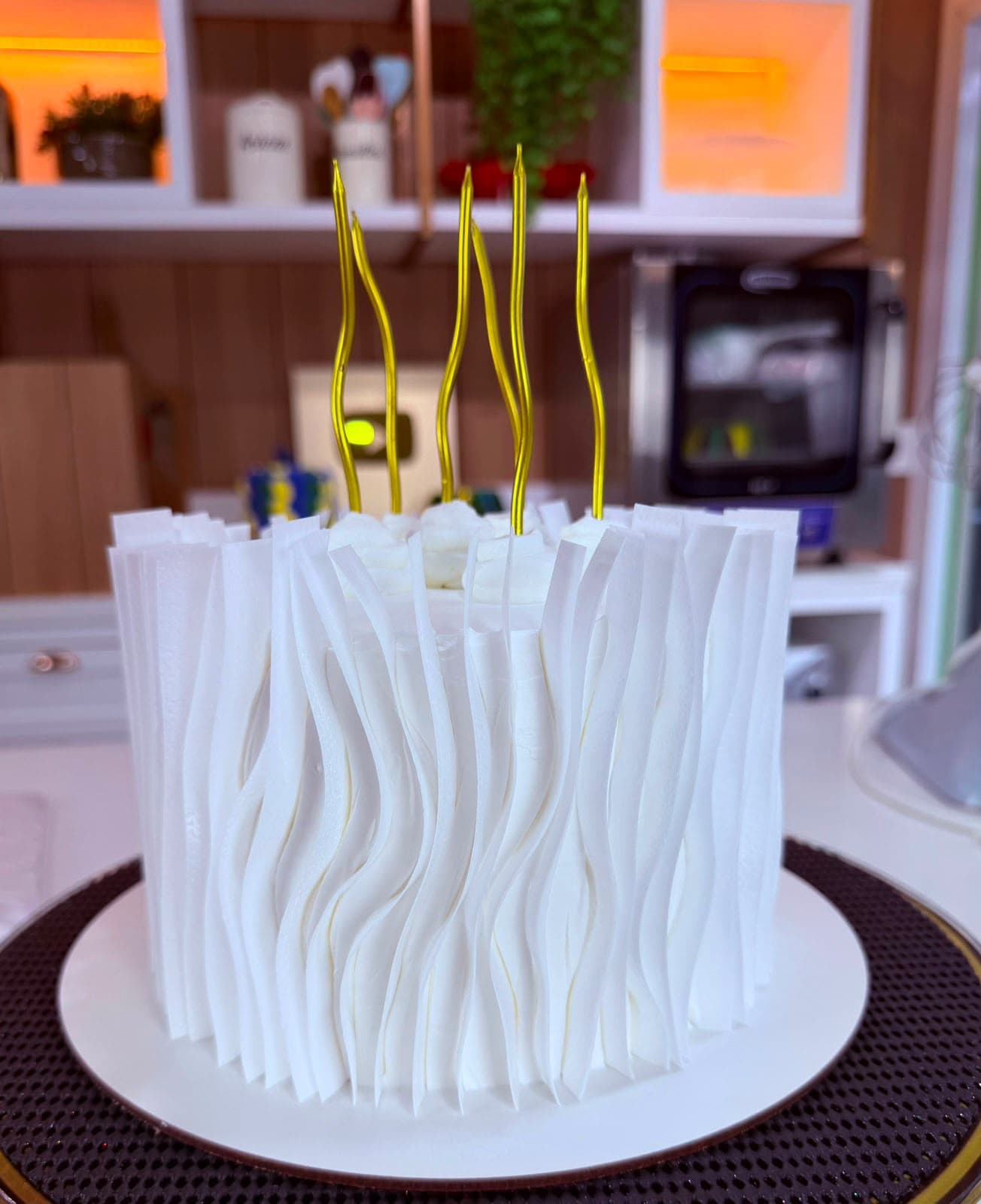 Bolo branco com babados verticais e velas douradas