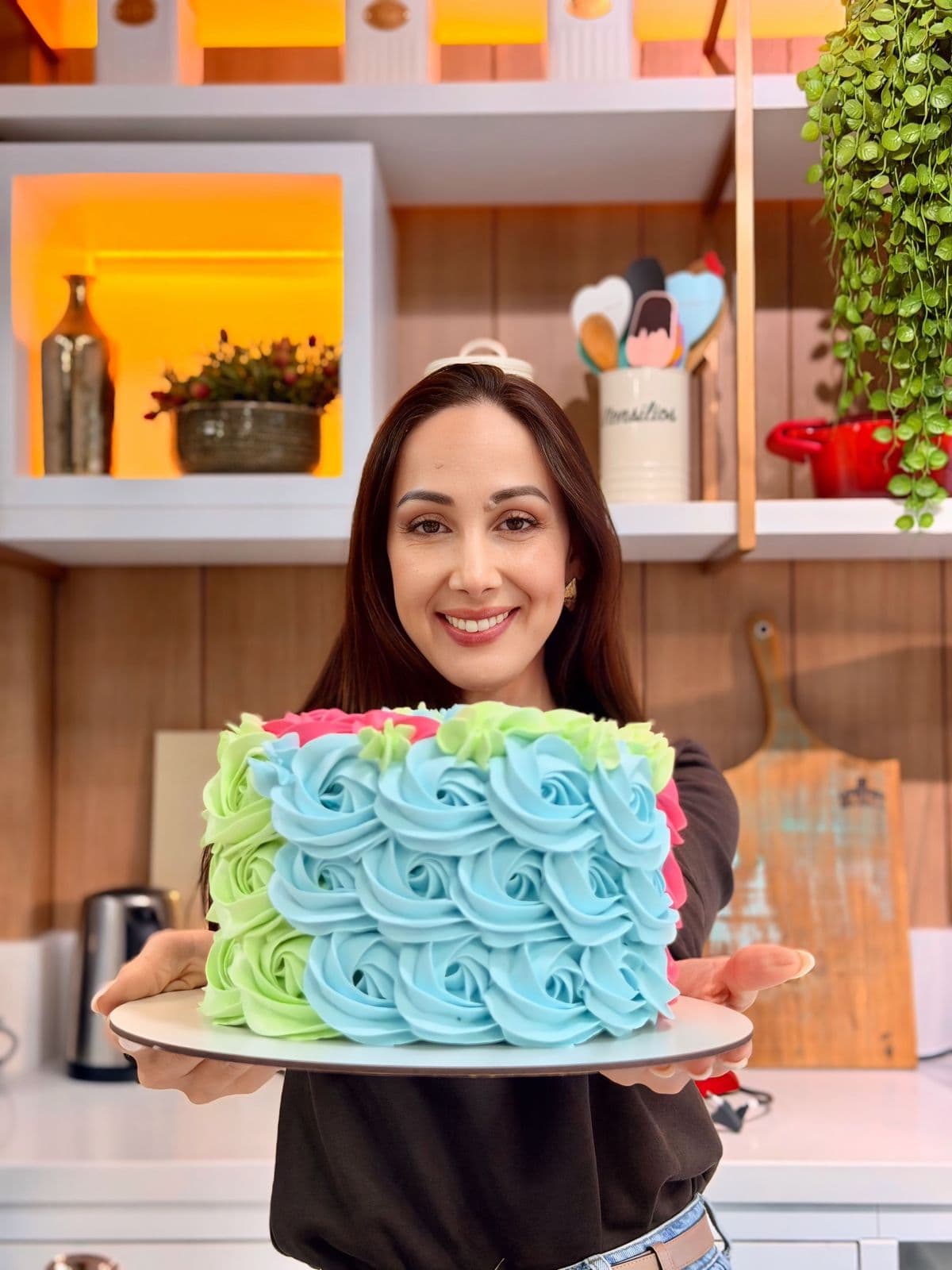 Marrara Bortoloti segurando um bolo decorado com rosetas coloridas de chantilly