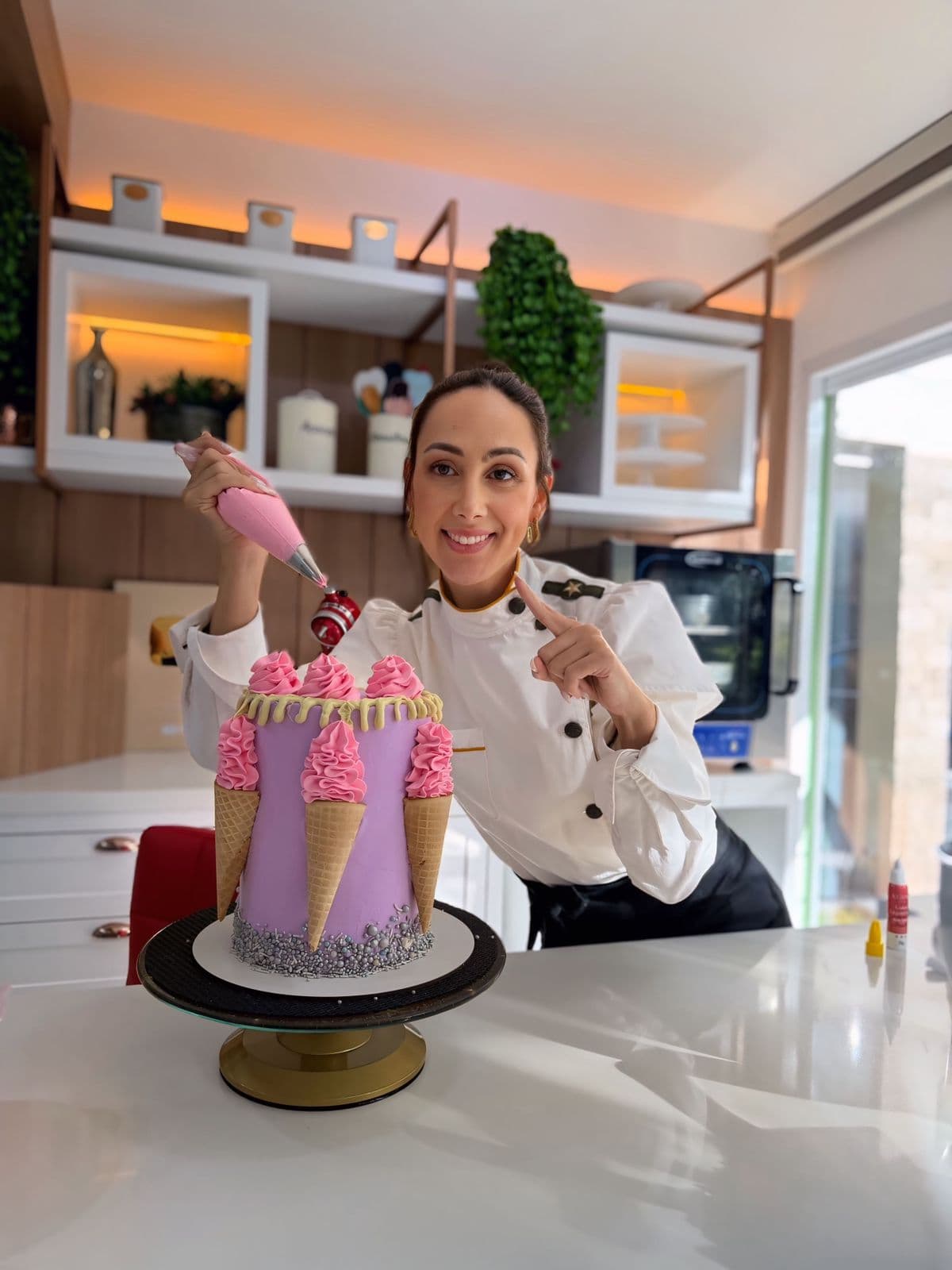 Confeiteira ao lado de um bolo lilás decorado com casquinhas